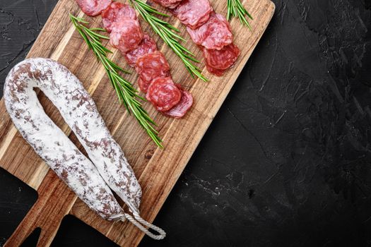 Fuet salami wurst cut in slices and whole sausage on black background, flat lay with copy space