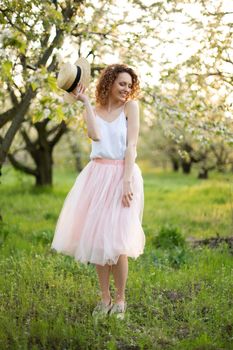 Young attractive woman with curly hair walking in a green flowered garden. Spring romantic mood