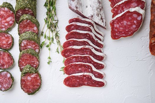 Variety of dry cured fuet and chorizosalami sausages, whole and sliced on white textured background, topview