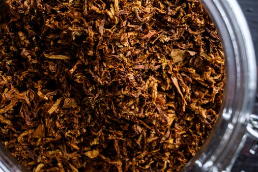 close-up Cigar and pile of Cut tobacco leaves of Dried tobacco in glass jars on rustic wood dark table top view overhead