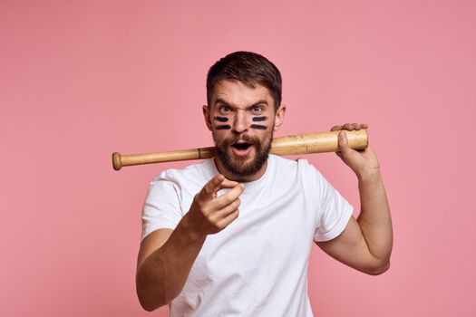 Emotional man with a baseball bat in his hand on a pink background and black lines on the face of the model grimace