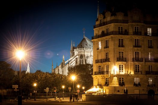 Notre Dame de Paris cathedral at night. Deep blue sky in background, typical parisian house in foreground. Paris, France, Europe.