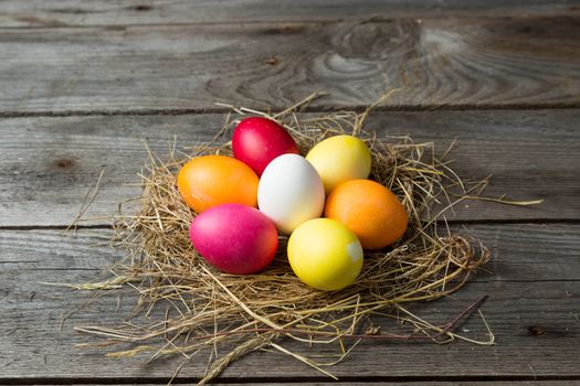 .Painted easter eggs in a makeshift straw nest on a wooden background