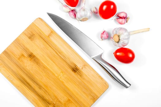 Closeup image of chief knife , garlic and tomato on white table