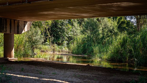 A Picturesque Creek Running Under A Bridge Used By Families To Cool Off From The Summer Heat