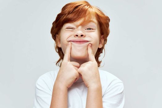 Cheerful red-haired boy grimaces Hands near face cropped view studio