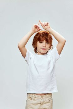 Red-haired boy holding his hands above his head showing upward white t-shirt Copy Space