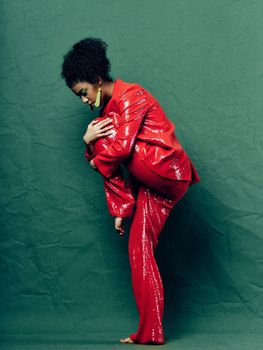 A woman in a shiny red suit bent her leg towards her jewelry