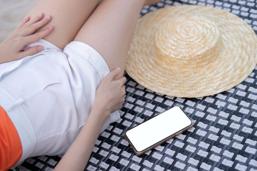 Woman lying on sunbath bed with mobile phone and blank white scr