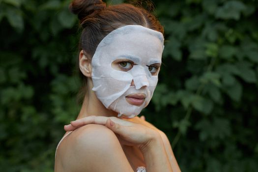 Nice woman Holds hand on shoulder side view anti-aging mask bare shoulders leaves in the background