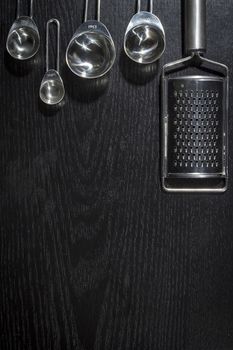 Metal measuring spoons and grater on black wooden background