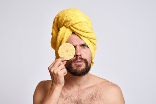 man with a yellow towel on his head bare shoulders sponge clean skin facial care light background