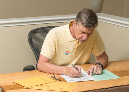Senior caucasian man sitting at his desk and completing absentee voting ballot