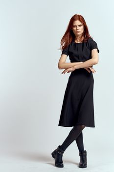 A woman in a black dress on a light background and pantyhose shoes red hair and pose in full growth