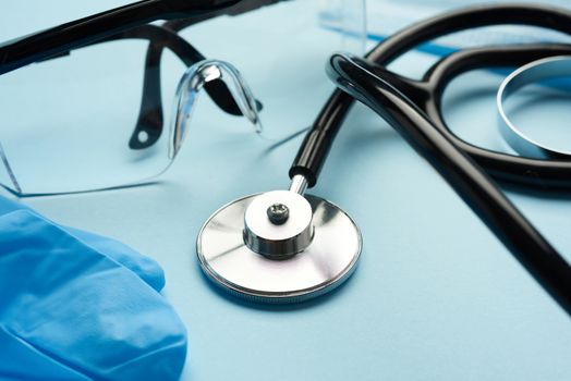 black medical stethoscope, plastic safety goggles on blue background, close up