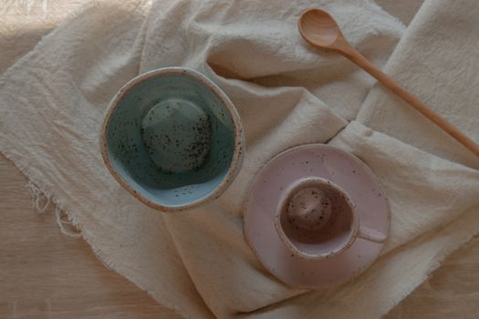 Blue and pink ceramics mugs handmade with wooden spoon on white calico. Home decor. Space for text. No focus, specifically.