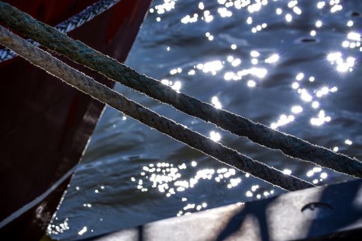 Mooring line of a trawler in backlight with water reflections