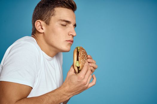 man with hamburger and white t-shirt blue background emotions gesturing with hands Copy Space. High quality photo