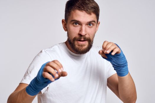 A sportive man in a white T-shirt boxing bandages on his hands practicing blow exercises improving skills