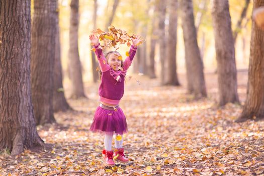 Cute little girl in autumn park with orange and yellow color leaves