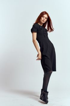 A woman in a black dress on a light background and pantyhose shoes red hair and pose in full growth