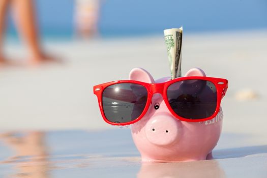 Pink pig moneybox in red sunglasses on the beach