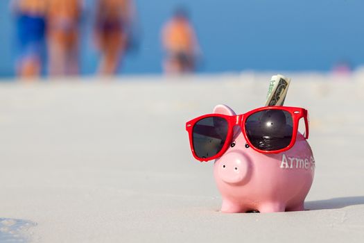 Pink pig moneybox in red sunglasses on the beach