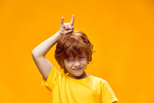 Expressive red-haired boy holding two fingers above the head of the horns