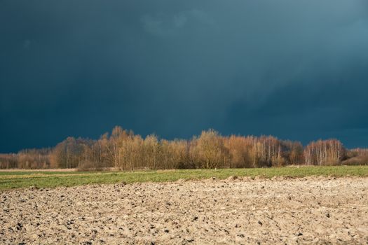 Ploughed field, autumn forest and dark clouds on the sky