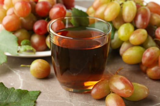 Glass of juice and plate with grape on gray background