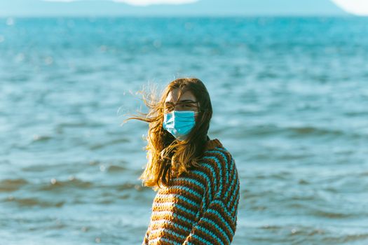 Young woman on a jersey on the beach using a surgical mask on moody tones