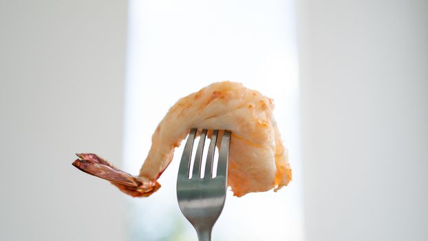 Cooked shrimp on fork on white blurred background.