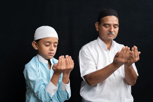 Muslim father and son in medical mask praying or performing Salah o protect from coronavirus or covid-19 by sitting.
