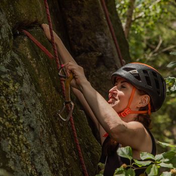 Woman clipping in quick draw carabiner while rock climbing a bou