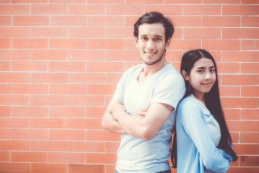 Young couple asian man and woman attractive stand arm  crossed and smile while back to back on brick wall background with romantic, boyfriend and girlfriend with confidence, romantic concept.