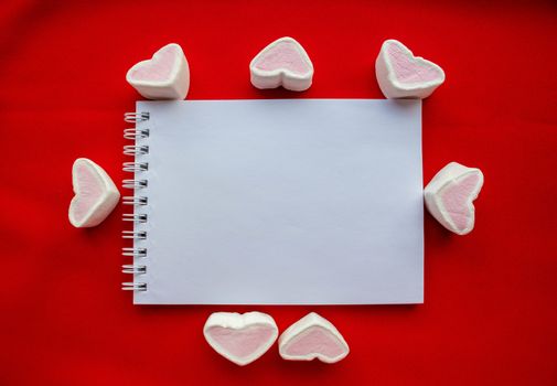 Hearts - marshmallow candies and Notepad, isolated on a red background.