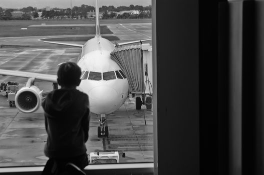 A child is sitting and looking for a plane at the airport in monochrome tone