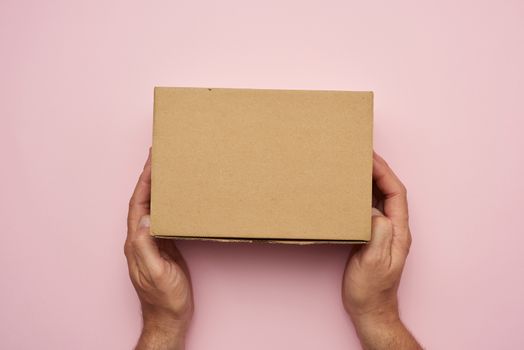 two female hands hold closed brown paper box on a pink backgroun