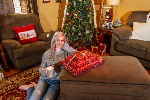 A lovely young Blonde model enjoys the holiday season at home with a Christmas tree and presents