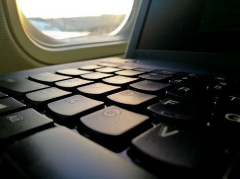 Laptop computer keyboard near airplane cabin window seat working