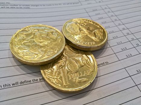 Three gold coins of Australian dollars on invoice sheet