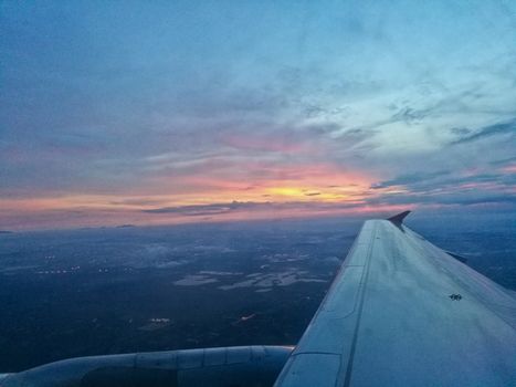 Scene of sun set from window seat of airplane flying above cloud