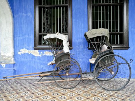 Old vintage traditional rickshaws in front of blue building in P