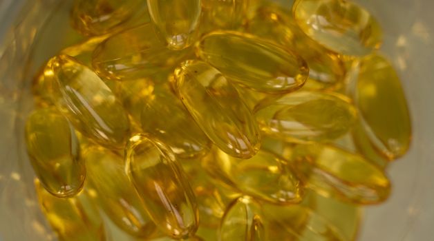 Extreme close up of fish oil orange yellow softgels capsules fish oil omega 3 or omega 6, omega 9, vitamin A, vitamin D, vitamin E background. Healthy vitamins product concept.