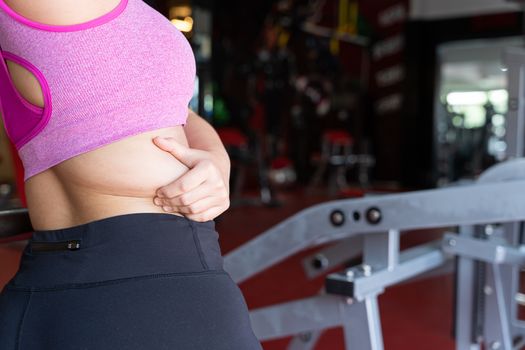 Fat woman holding excessive fat belly lower back, overweight fatty belly at fitness gym. Diet lifestyle, weight loss, stomach muscle, healthy concept.