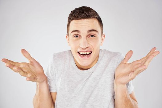 Man in a white t-shirt emotions gestures with hands close-up cropped view light background