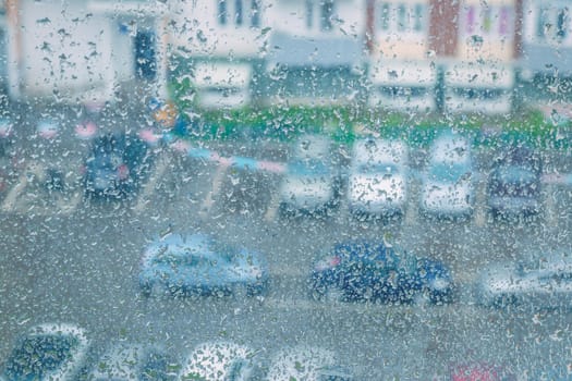 View through a rainy window on a blurred house and car parking. 