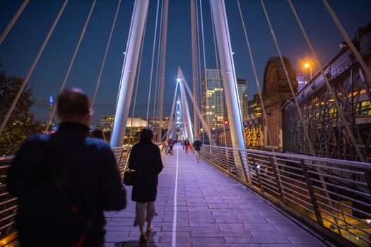 Pedestrians walking on a white bridge above the River Thames during nighttime