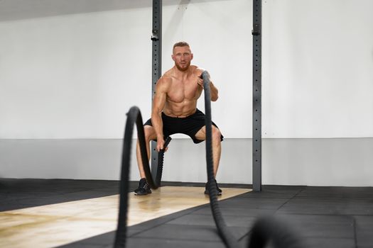 Gym battle rope man stamina training Athlete guy fitness exercising endurance indoor workout.