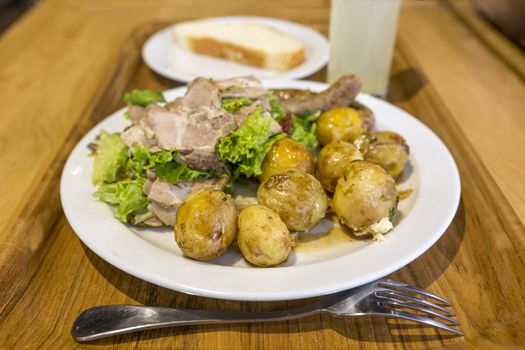 A plate with young potatoes and meat is standing on a tray